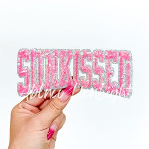 May include: Pink sequin patch with the word "SUNKISsed" in white letters.