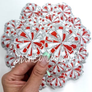 May include: A close-up of a pile of red, white, and silver glitter pom-poms. The pom-poms are about 2 inches in diameter and have a sparkly finish.