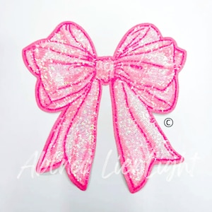 May include: A large pink sequined bow with a shiny iridescent finish. The bow is a decorative embellishment for clothing or crafts.