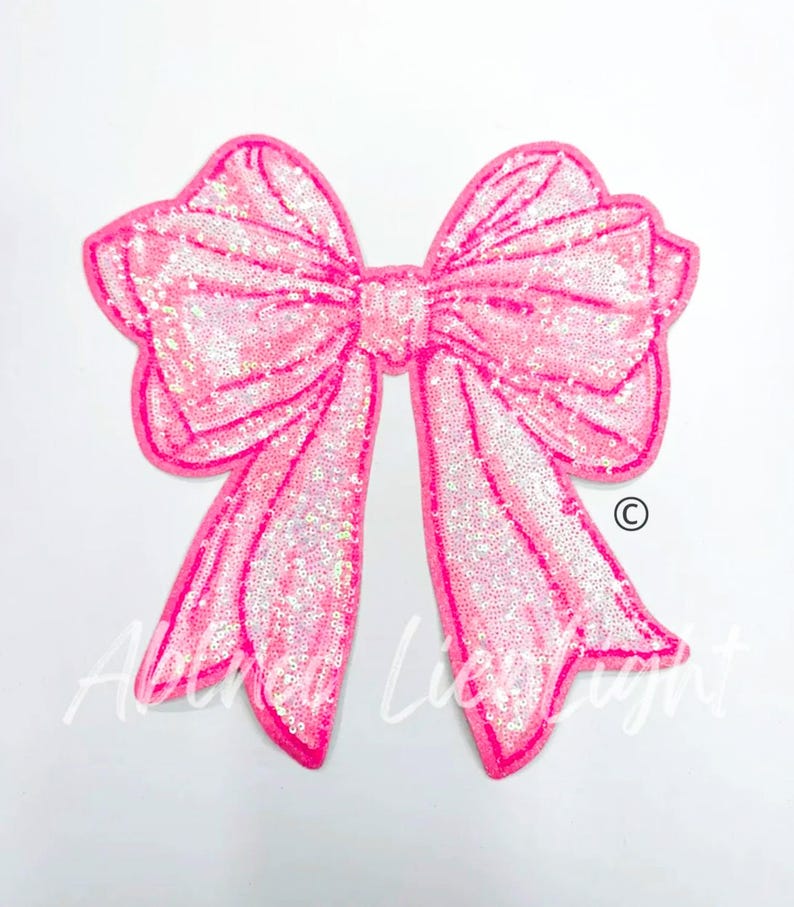 May include: A large pink sequined bow with a shiny iridescent finish. The bow is a decorative embellishment for clothing or crafts.