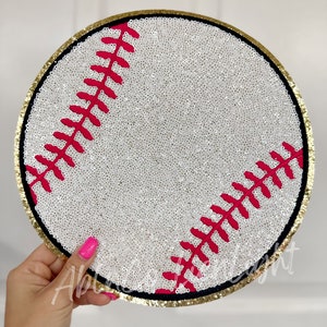 May include: A white baseball with red stitching and a gold trim. The baseball is covered in sequins.