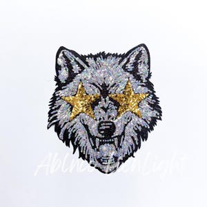 May include: A sequined wolf head patch with gold star-shaped sunglasses. The wolf's fur is silver and black, with a detailed design. The patch is likely for clothing or accessories.