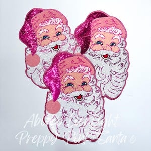May include: Three pink and white Santa Claus face iron-on patches. The Santa faces have white beards and pink hats with sequins.