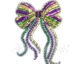 May include: A large, sequined bow in the colors of Mardi Gras: gold, green, and purple. The bow has long, flowing tails and is heavily embellished with sequins. The design is symmetrical and festive, perfect for celebrations.