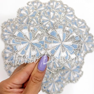 May include: A stack of blue and silver glitter iron-on patches in the shape of a flower. The patches have a geometric design and are perfect for adding a touch of sparkle to any project.