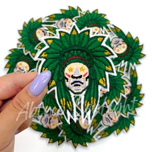 May include: A pile of green and gold embroidered iron-on patches featuring a cartoon Native American chief wearing a headdress.