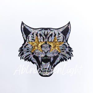 May include: Black and white sequined iron-on patch of a tiger's face with gold star-shaped sunglasses.