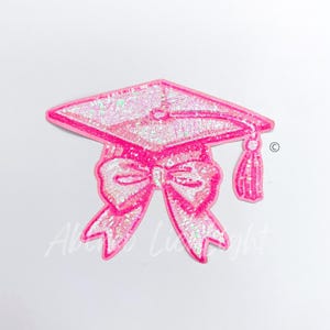 May include: Pink graduation cap with a bow and tassel. The cap and bow are covered in iridescent sequins.