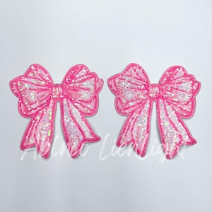 May include: Two pink sequined bow patches. The bows are made of iridescent sequins and have a white satin ribbon.