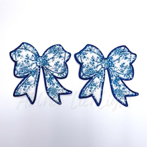 May include: Two blue and white bow-shaped fabric patches with a floral pattern. The bows are decorated with sequins.