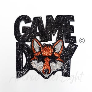 May include: Black sequined patch with the words "GAME DAY" and a fox face. The fox has orange and white details. The patch is on a white background.