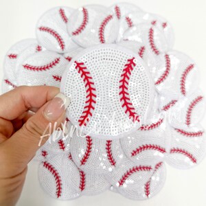 May include: A pile of white and red baseball-shaped sequins with red stitching. The sequins are arranged in a circular pattern.