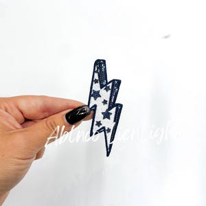 May include: A white lightning bolt patch with blue outline and blue glitter stars.