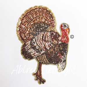 May include: A brown and gold sequined turkey applique. The turkey has a red head and wattle. The applique is perfect for adding a festive touch to crafts and projects.