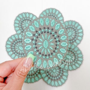 May include: Set of four gray and teal embroidered coasters with a circular design. The coasters are made of a soft, textured material and have a delicate, intricate pattern.