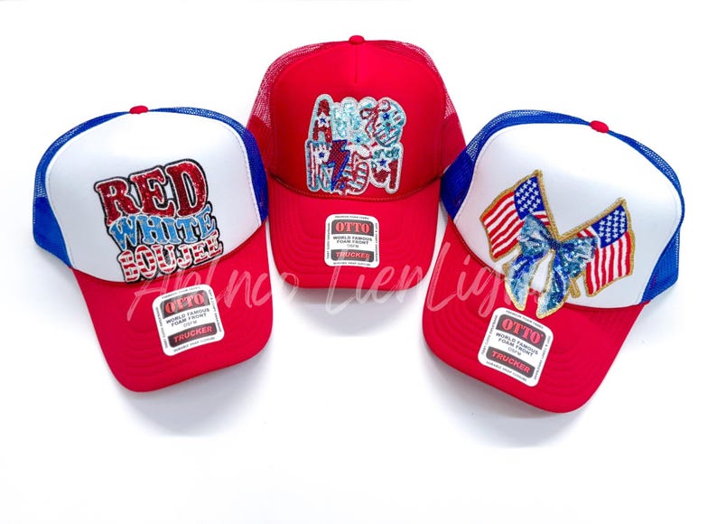 May include: Three red, white, and blue trucker hats with different patriotic designs. The first hat has the words "Red White Blue" in red, white, and blue letters. The second hat has the word "America" in red, white, and blue letters. The third hat has two American flags with a blue bow in the center.
