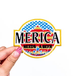 May include: An embroidered patch with a red, white, and blue American flag design. The patch is yellow and has the text "MERICA NEEDS A BEER" on it.