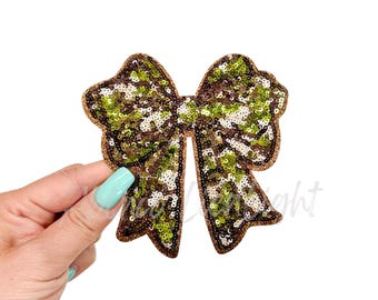Puede incluir: Un gran lazo de lentejuelas verde y marrón con un patrón de camuflaje. El lazo está hecho de lentejuelas y es perfecto para agregar un toque de brillo a cualquier proyecto.