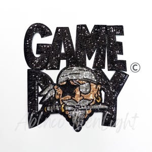 May include: Black sequined patch with the words "GAME DAY" and a pirate graphic. The pirate has a gold earring, eye patch, and a bandana. The patch is on a white background.