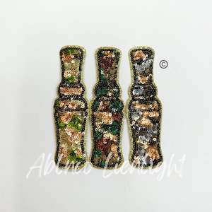 May include: Three sequined patches in a camouflage pattern, each shaped like a hunting call. The patches are gold, green, and brown.