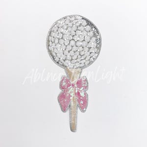 May include: A silver sequin lollipop with a pink sequin bow.