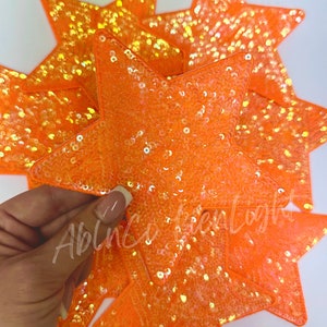 May include: A group of orange star-shaped sequins patches. The sequins are iridescent and have a shimmery finish.
