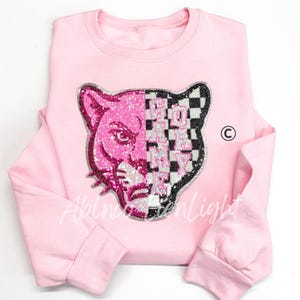 May include: Pink sweatshirt with a sequined panther design. The panther is split, with one half in pink sequins and the other in a black and white checkered pattern. The text "GO PINK" is also in sequins.