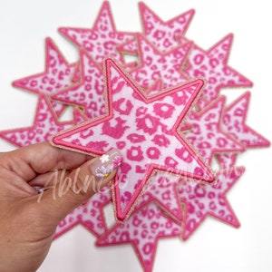 May include: A stack of pink and white star-shaped fabric patches with a leopard print design and gold glitter trim.