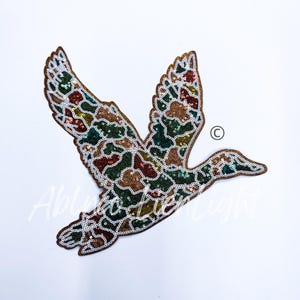 May include: A brown, green, and gold sequined applique of a flying duck. The duck is outlined in white.