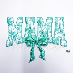 May include: A turquoise blue fabric patch with the word "MAMA" in white letters with a turquoise floral pattern. A turquoise blue sequin bow is centered below the word.