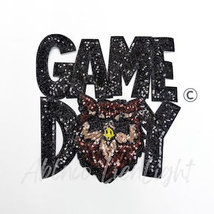 May include: Black sequined "GAME DAY" patch with a brown and black wolf design. The patch features a wolf's face with yellow eyes and is set against a white background. The text is in large, bold letters.