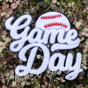 May include: White felt applique with the words "Game Day" in a black outline. A red and white baseball is above the words.