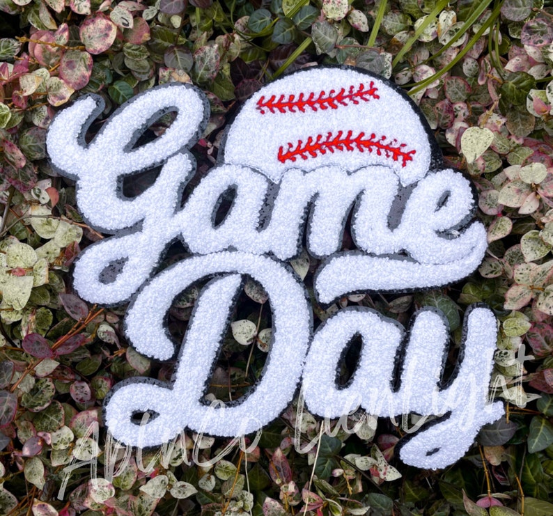 May include: White felt applique with the words "Game Day" in a black outline. A red and white baseball is above the words.