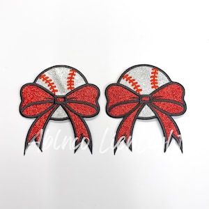 May include: Two red glitter bows with a white baseball in the center. The bows are black outlined and have a silver glitter finish.