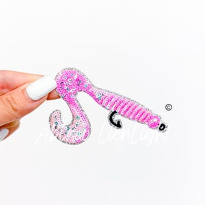 May include: A pink sequined hair curler patch with a silver glitter outline. The curler has a curved handle and a black accent. The patch is on a white background.