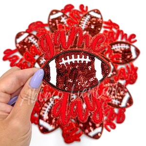May include: A set of red and white iron-on patches with the words "game day" and a football design. The football is made of red sequins.