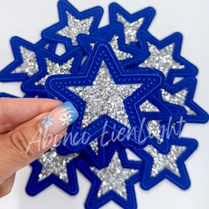 May include: A set of ten blue star-shaped patches with silver glitter. Each star has a blue outline and a white center.