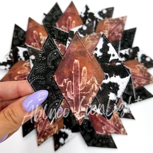 May include: A set of 12 diamond-shaped fabric patches with a southwestern desert theme. Each patch features a cactus, mountains, and a sunset sky in shades of brown, orange, and red. The patches are surrounded by black and white cowhide print fabric.