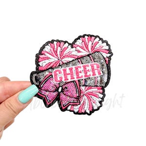 May include: A pink and white cheerleading pom pom with a silver and black megaphone with the word "CHEER" in pink letters. The megaphone has a pink bow on it.