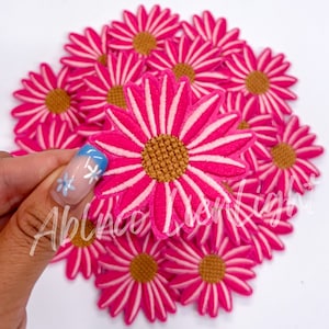 May include: A pile of pink felt daisy flower patches with white stripes and a brown center.