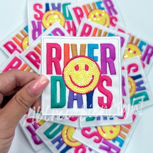 May include: A stack of colorful iron-on patches with a smiley face and the text "River Days".