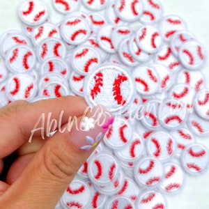 May include: A large pile of white and red baseball-themed iron-on patches. The patches are about 1 inch in diameter and feature a white background with a red baseball stitch design.