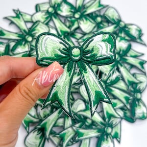May include: A pile of green and white embroidered fabric bow patches. The bows are about 2 inches wide and have a satin finish.