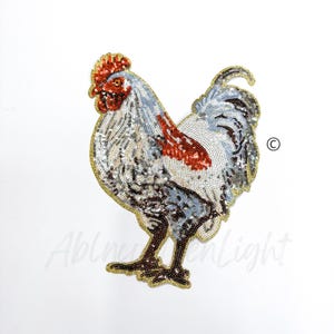 May include: A white, red, and gold sequined rooster applique. The rooster is standing with its head turned to the left. The applique is perfect for adding a touch of whimsy to clothing, bags, or home decor.
