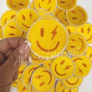 May include: A group of yellow embroidered iron-on patches with a smiley face and a lightning bolt design. The patches have a white outline.