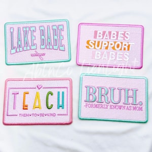 May include: Four embroidered iron-on patches with different sayings. The patches are pink with light blue, green, and yellow lettering. The sayings are "LAKE BABE", "BABES SUPPORT BABES", "TEACH THEM TO BE KIND", and "BRUH. FORMERLY KNOWN AS MOM".