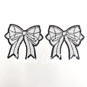 May include: Two white sequin bow patches with black outlines. The bows are in a classic shape with a center knot and two loops.