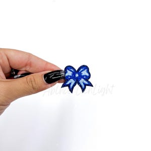 May include: A small blue bow with white stitching, perfect for adding a touch of whimsy to crafts and projects.