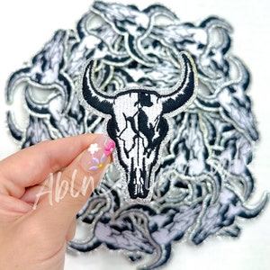May include: A pile of silver glitter iron-on patches featuring a white and black bull skull design.