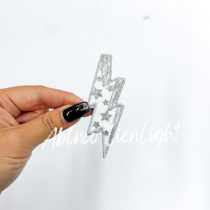 May include: A white lightning bolt iron-on patch with silver glitter stars.